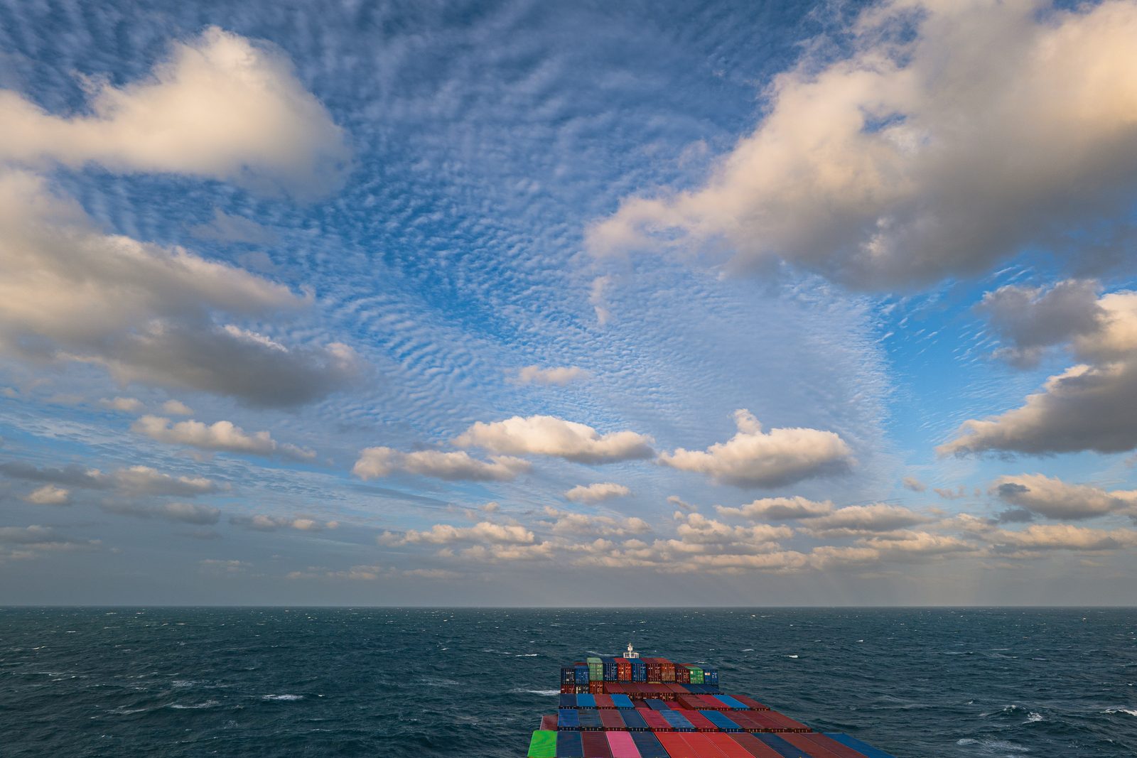 Wide sky with drifting clouds over a choppy sea, ship's stern in view