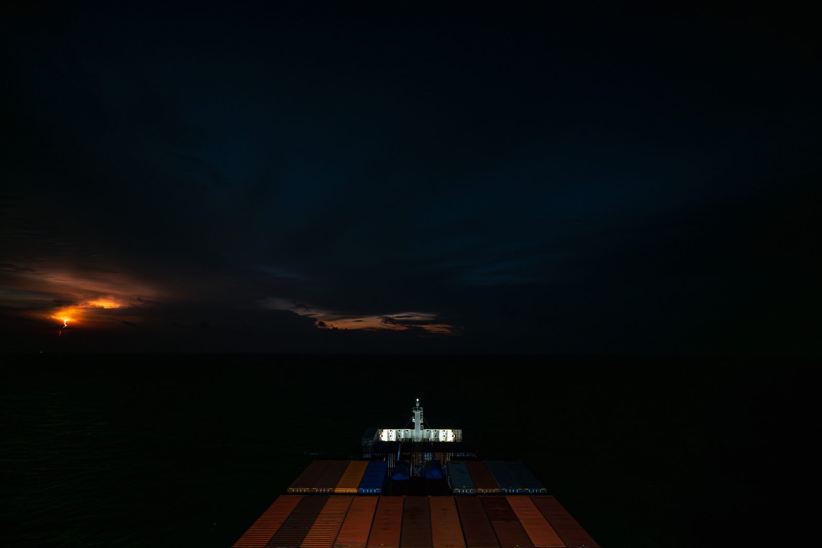 A lit ship on the dark sea at night with distant lightning on the horizon
