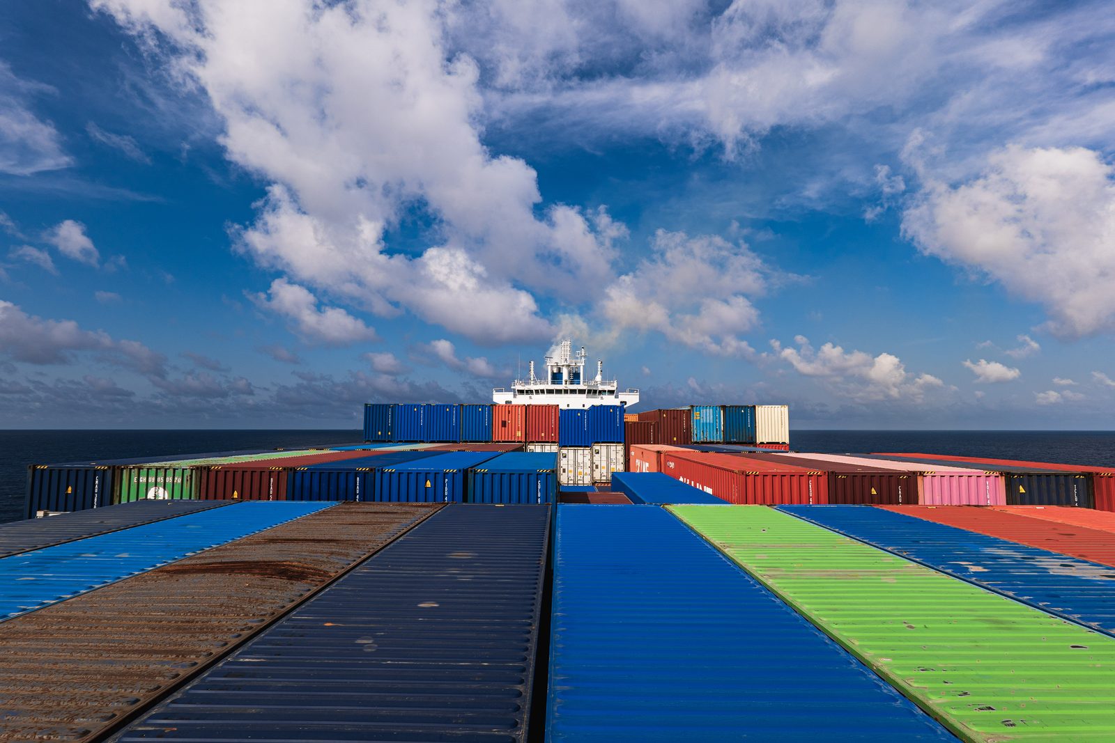 Colorful containers stretching toward the bridge, with the funnel's exhaust mixing into the clouds