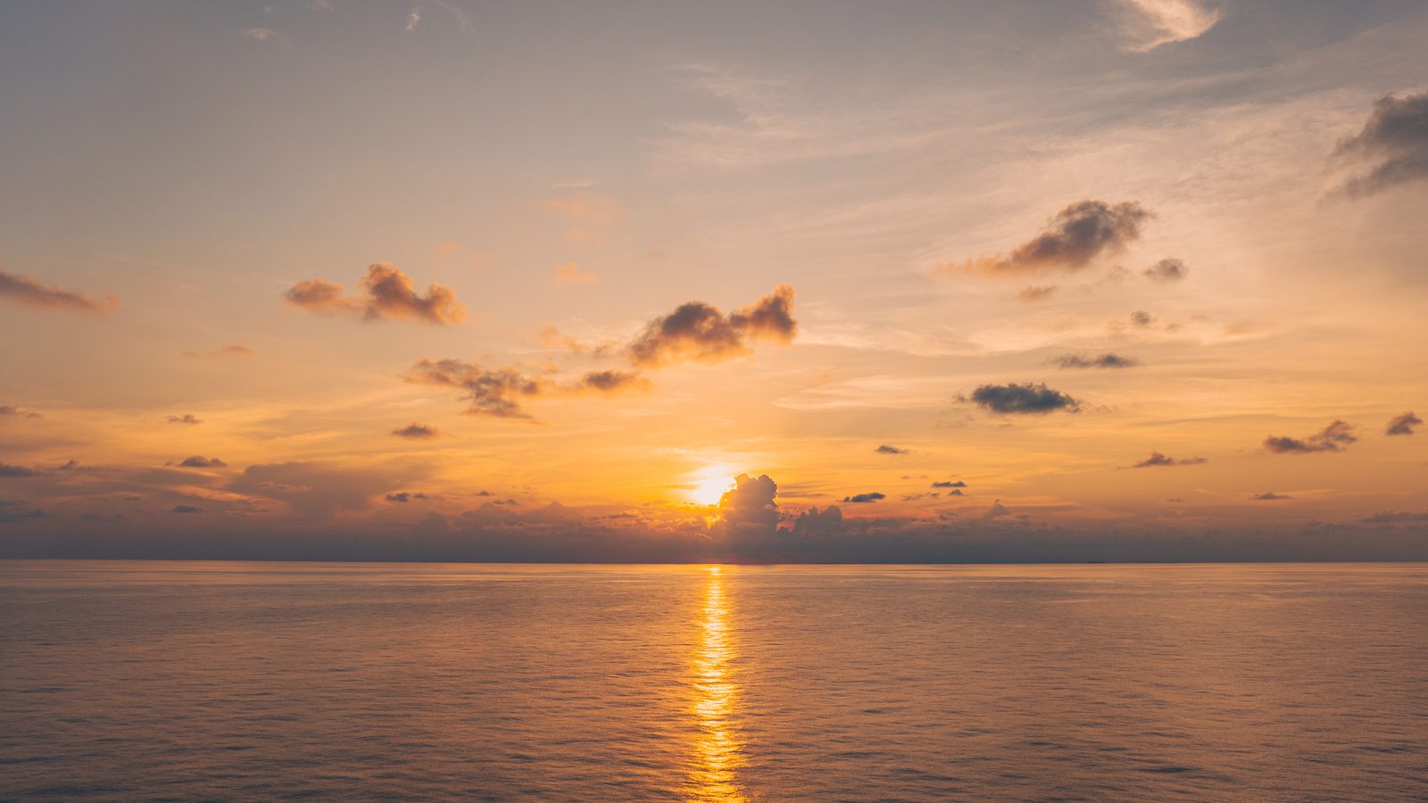 Sunset over open water, ships silhouetted on the horizon